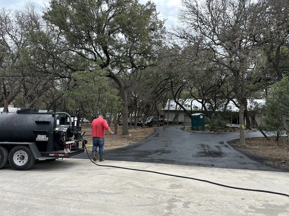 A Lonestar Construction Industries crew member applying seal coat to a residential asphalt driveway in the San Antonio area